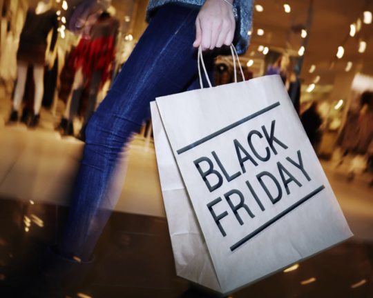 paper shopping back with black friday written on it held by shopper